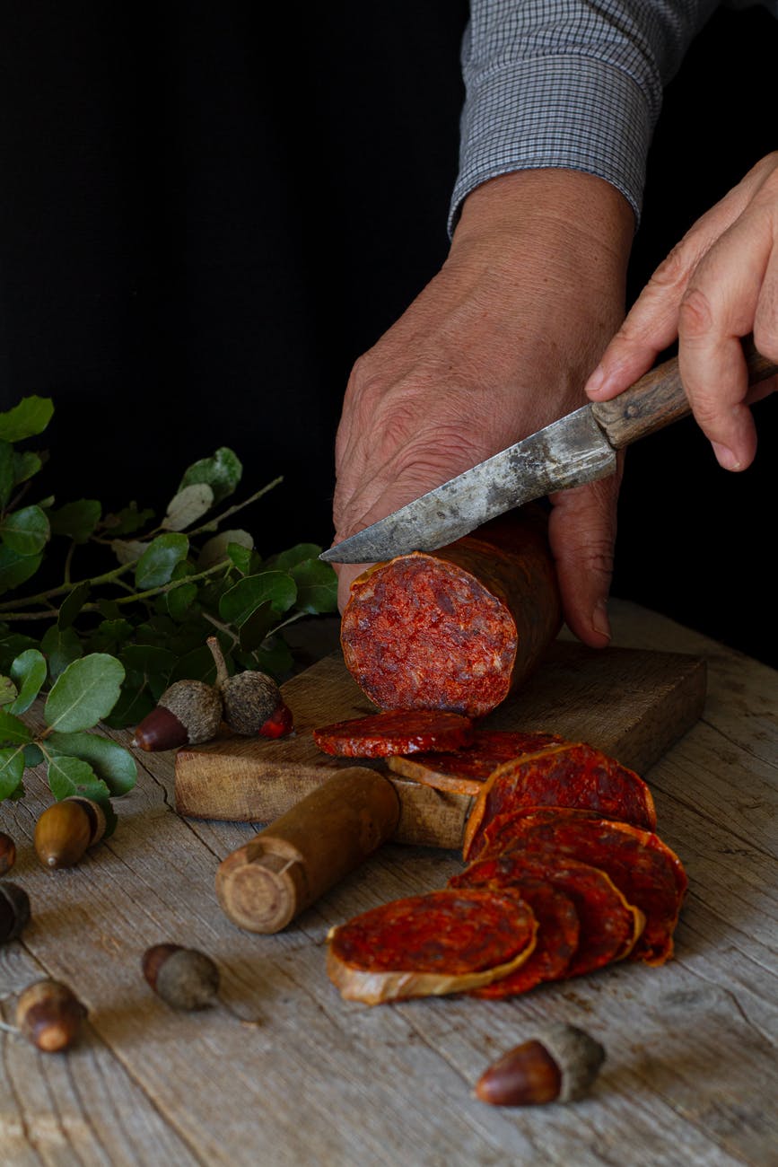 a person cutting processed meat on a wooden chopping board