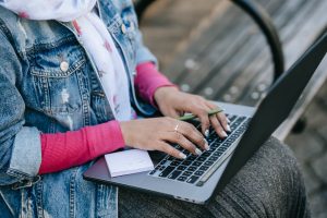 crop lady typing on portable laptop with pen in hands