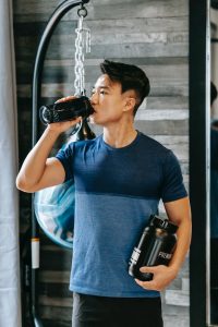 asian athlete drinking water standing with bottle sports supplements