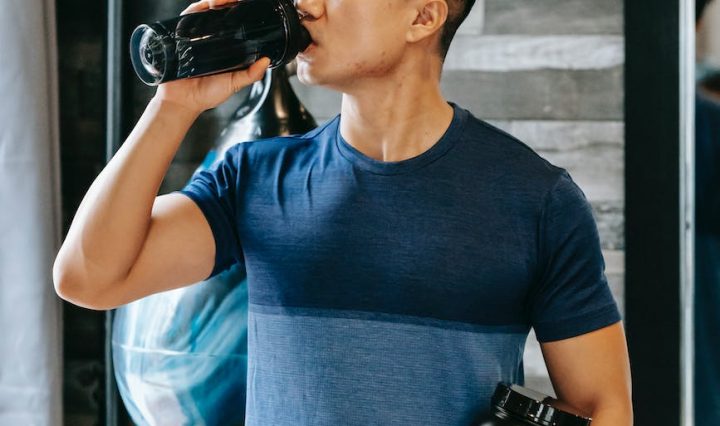 asian athlete drinking water standing with bottle sports supplements