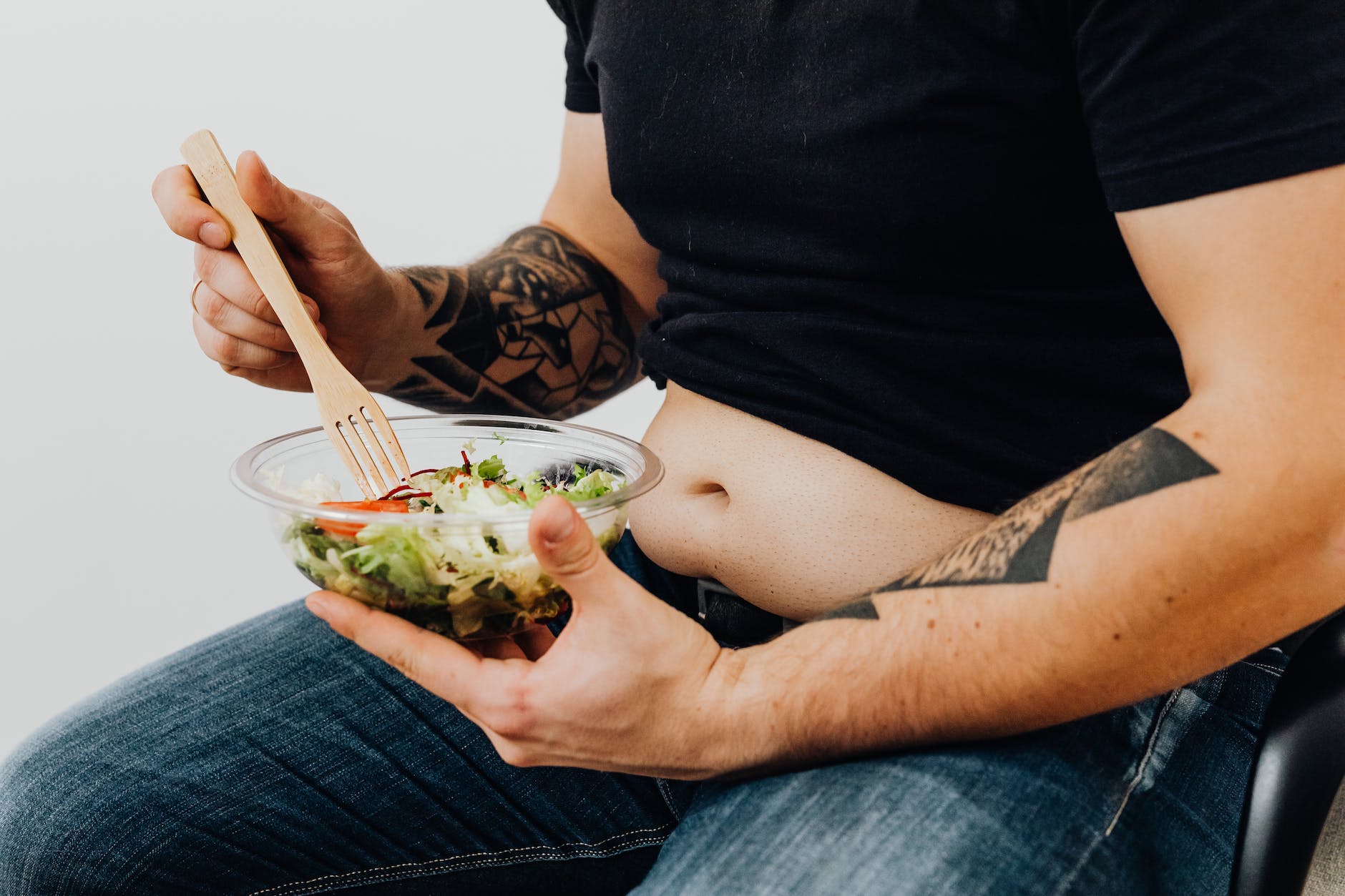 close up shot of a tattooed man holding a fresh vegetable salad