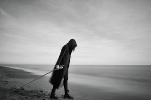 woman in black cloak with fishing pole standing in beach