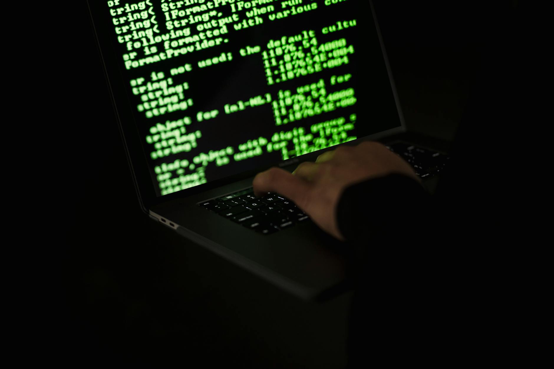 crop hacker typing on laptop with information on screen